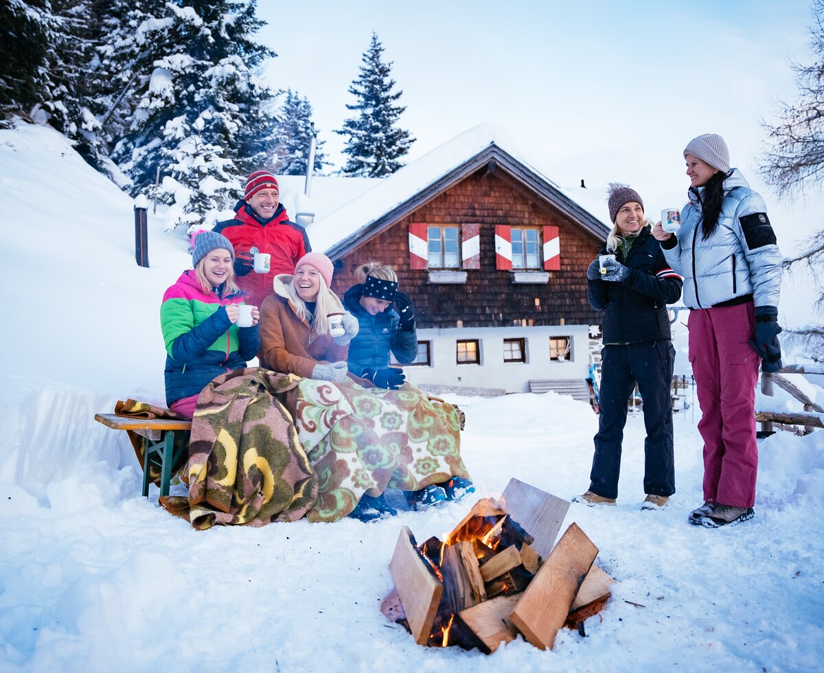 Freunde sitzen bei der Feuerstelle im Schnee vor der Hütte | © Urlaub am Bauernhof Kärnten/ Daniel Gollner