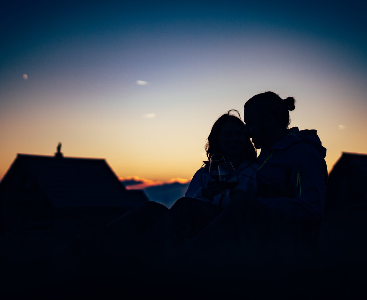 Paar sitzt im Gras im Sonnenuntergang vor der Almhütte | © Urlaub am Bauernhof/ Daniel Gollner