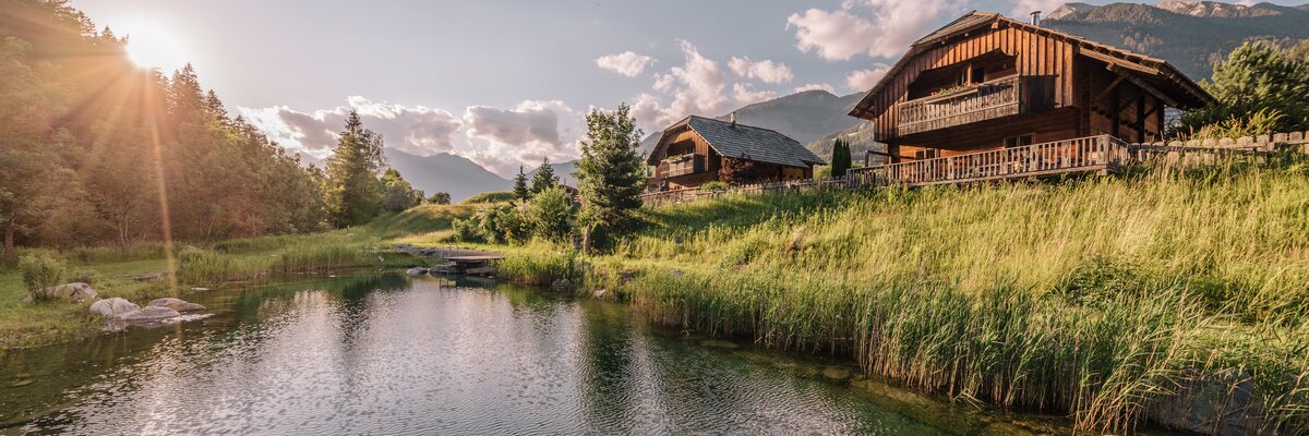 Badeteich mit Chalets des Landgut Moserhof im Hintergrund im Sonnenuntergang | © Daniel Waschnig / Urlaub am Bauernhof Kärnten