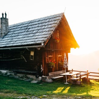 Die Almhütte scheint im Morgenlicht bei der aufgehenden Sonne in Kärnten | © Urlaub am Bauernhof Kärnten / Daniel Gollner