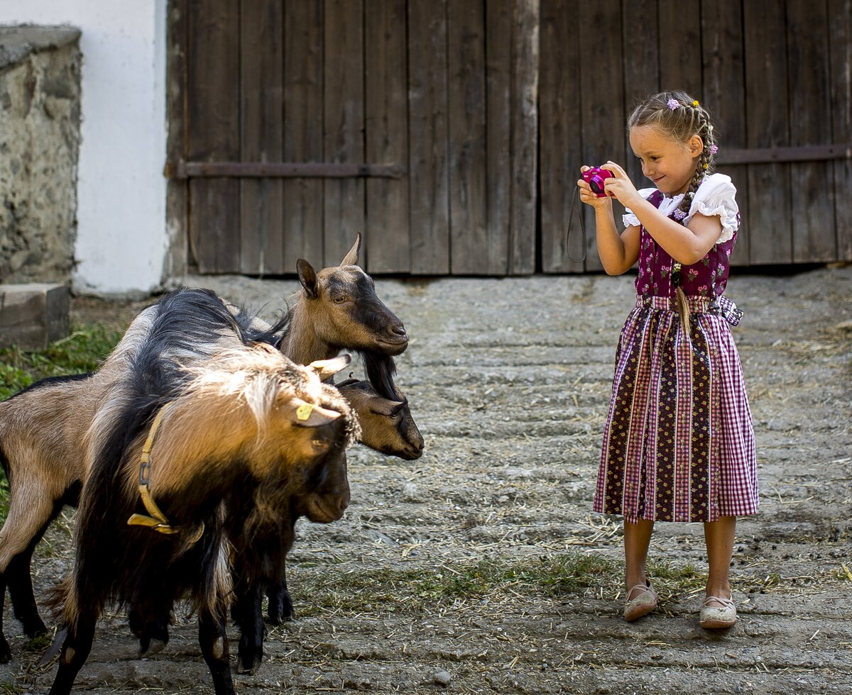 Mädchen im pinken Dirndl fotografiert Ziegen mit Spielzeugkamera | © Urlaub am Bauernhof Kärnten / Tom Lamm