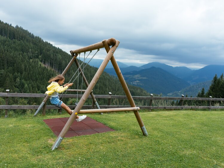 Ein Mädchen ist am Schaukeln. Im Hintergrund sieht man eine schöne Berglandschaft. | © Urlaub am Bauernhof Kärnten/ Angelina Tschische