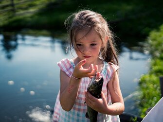 Mädchen hält Fisch in der Hand am Teicht | © Urlaub am Bauernhof Kärnten/ Daniel Gollner