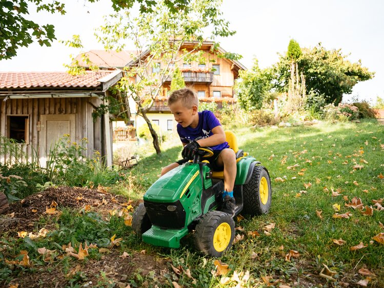 Bub sitzt am Spielzeugtraktor auf der Wiese | © Urlaub am Bauernhof Kärnten / Daniel Gollner