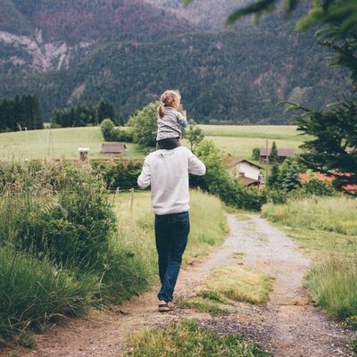 Mädchen sitzt auf den Schultern des Mannes und sie spazieren am Weg | © Urlaub am Bauernhof Kärnten / Daniel Gollner