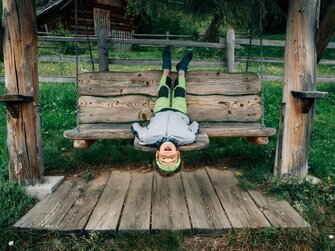 Bub liegt kopfüber auf der Schaukel | © Urlaub am Bauernhof Kärnten/ Daniel Gollner