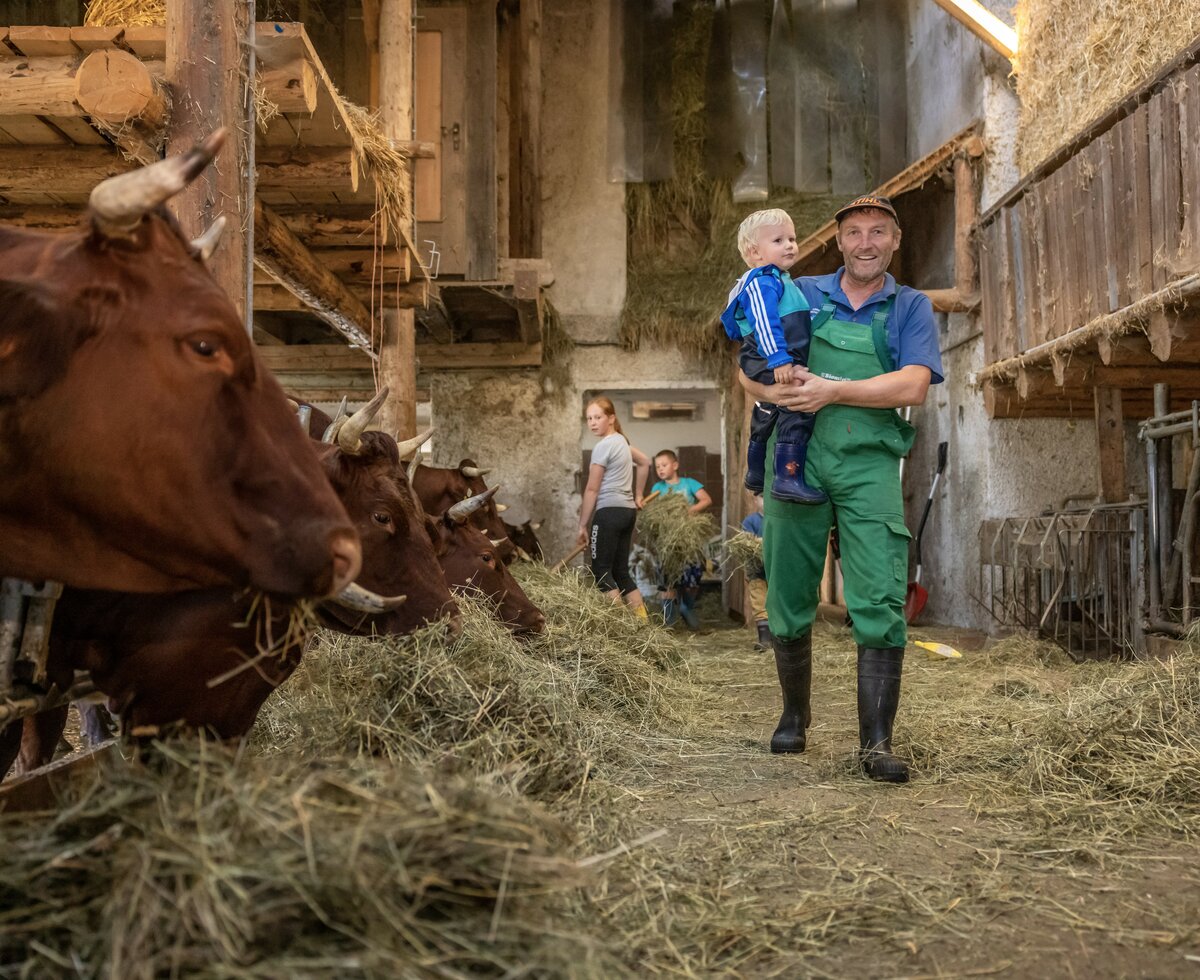 Bauer trägt Bub durch den Stall | © Landesverband Urlaub am Bauernhof Kärnten/ Achim Mandler