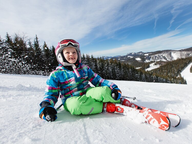 Kind sitzt mit Ski auf der Piste | © Niederösterreich Werbung / schwarz-koenig.at