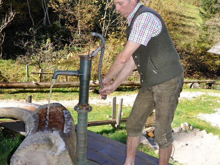 Mann pumpt an einem Brunnen frisches Quellwasser heraus | © Urlaub am Bauernhof Oberösterreich / Harald Puchegger