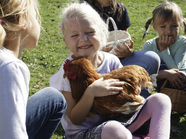 Kind hält ein Huhn auf dem Arm und streichelt es | © Urlaub am Bauernhof Oberösterreich / Harald Puchegger