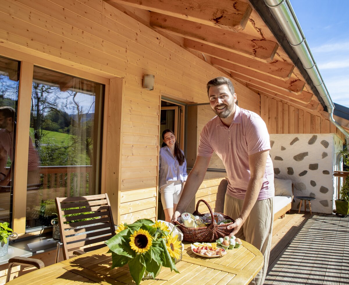 Mann richtet Frühstück auf der Terrasse für seine Partnerin an | © Urlaub am Bauernhof Oberösterreich / puremotions photography