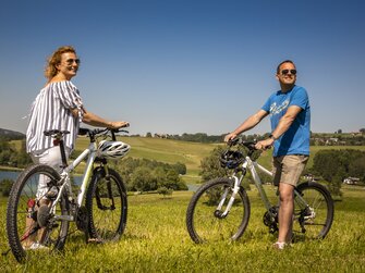 Paar steht mit Fahrrädern in der Wiese beim Irrsee | © Urlaub am Bauernhof Österreich / Bernd Suppan