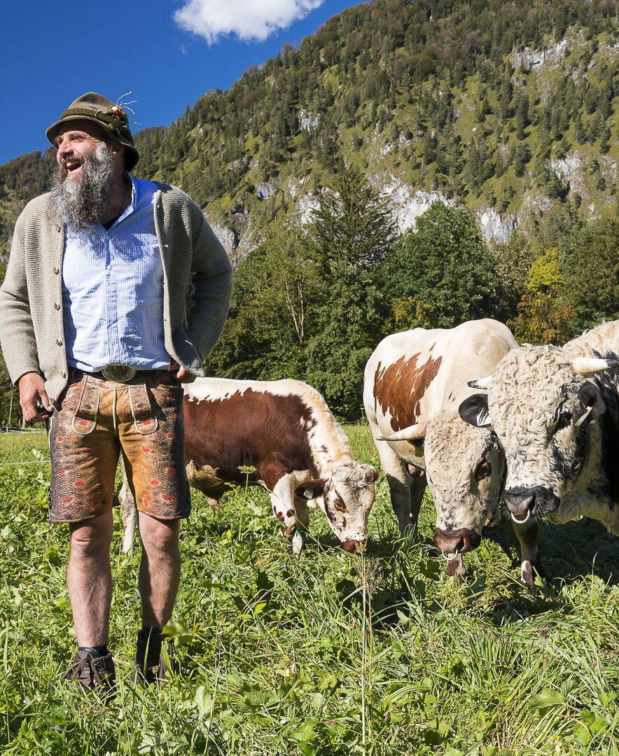 Bauer lacht auf der Wiese bei den Kühen | © Urlaub am Bauernhof / Uwe Grinzinger