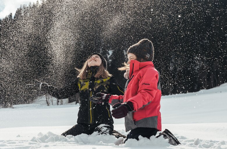 Kinder werfen Schnee in die Luft | © Urlaub am Bauernhof / Punkt und Komma Zwei fröhliche Personen spielen im verschneiten Winterwald, in dem die Schneeflocken in der Luft tanzen. Sie scheinen die Natur und die Winterlandschaft zu genießen. | © Urlaub am Bauernhof / Punkt und Komma