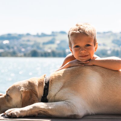 Ein Bub sitzt mit einem Hund am Steg | © Urlaub am Bauernhof / Punkt und Komma