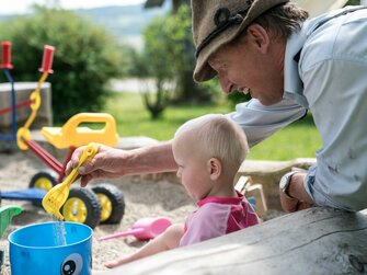 Bauer spielt mit einem Kleinkind in der Sandkiste | © Urlaub am Bauernhof im SalzburgerLand / Matthias Gruber