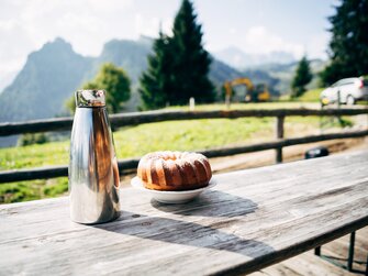 Ein Guglhupf und eine Thermoskanne mit Kaffee stehen auf dem Tisch vor der Almhütte. | © Urlaub am Bauernhof im SalzburgerLand / Daniel Gollner