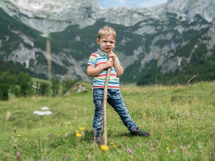 Ein kleiner Bub steht mit einem Haselnussstecken ausgerüstet auf der Almweide. | © Urlaub am Bauernhof im SalzburgerLand / Matthias Gruber