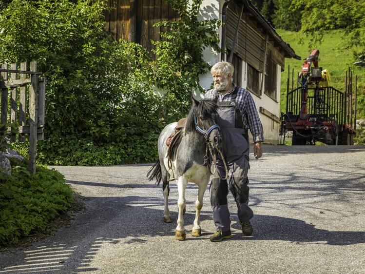 Bauer führt ein Pony über den Hof | © Urlaub am Bauernhof / Matthias Gruber