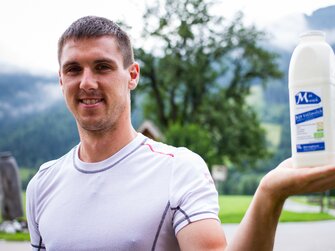 Jungbauer mit Milchflasche in der Hand am Zieferhof in Leogang, Salzburger Land | © Urlaub am Bauernhof / Matthias Gruber