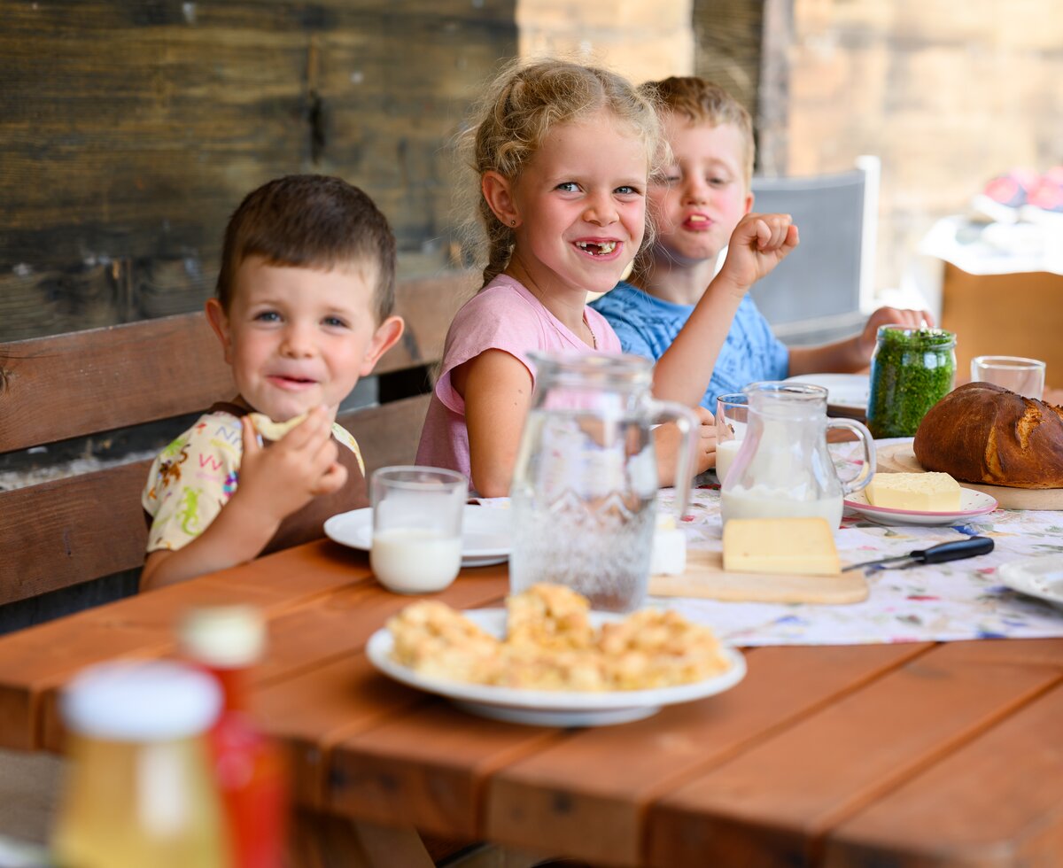 Ein Mädchen und zwei Jungs essen ein Jausenbrot auf der Terrasse, Pausshof in Kleinarl, Salzburger Land | © Urlaub am Bauernhof / punkt&komma