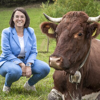 Helga kniet neben einer Kuh im Gras. | © Urlaub am Bauernhof im SalzburgerLand/Bernd Suppan