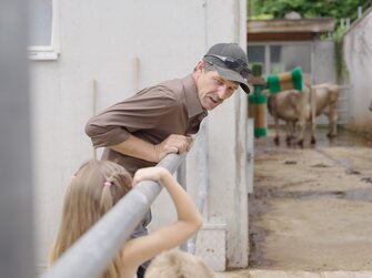 Mädchen beobachtet mit dem Bauern die Kühe im Laufstall | © Urlaub am Bauernhof | Daniel Gollner 