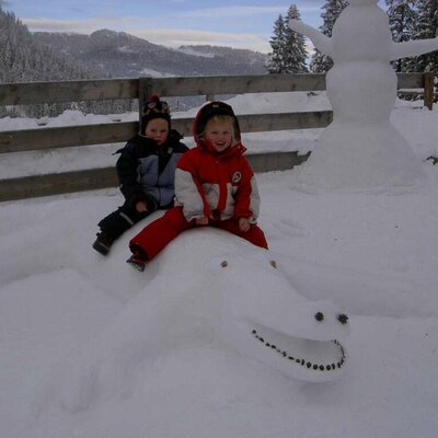 Kinder auf dem Schneekroko vor der Hütte