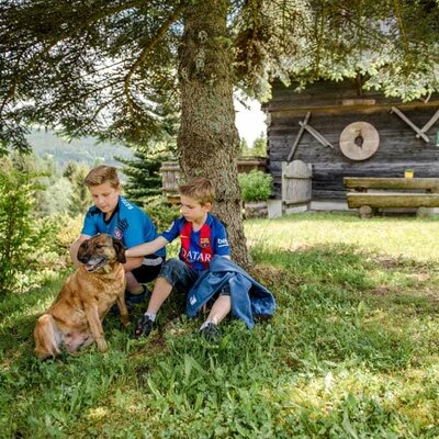 Kinder sitzen mit dem Hund vor einen Baum