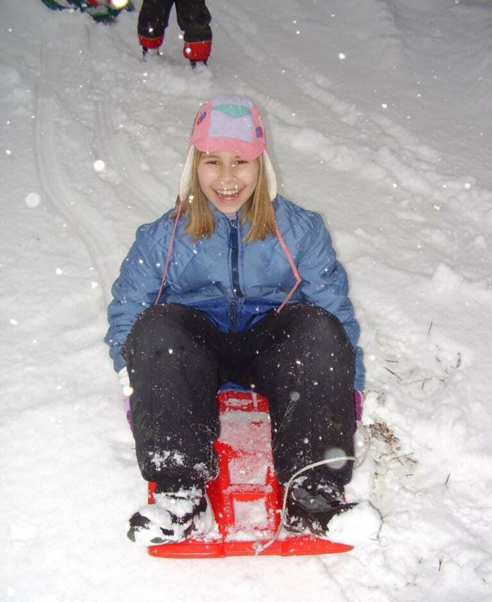 Mädchen fährt im Schnee auf einem roten Skibob.