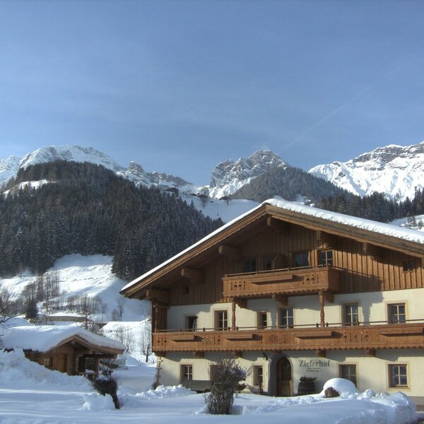 Außenansicht des Bauernhofs „Zieferhof“ mit schneebedecktem Dach und den verschneiten Bergen im Hintergrund. Außenansicht des Bauernhofs „Zieferhof“ mit schneebedecktem Dach und den verschneiten Bergen im Hintergrund.