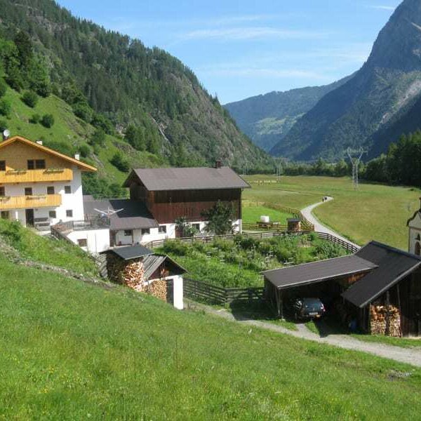 Blick von Süden (Hof im Gesamtblick): Räucherhaus, Heizlager mit Garage, hofeigene Kapelle mit Wohnhaus und Wirtschaftsgebäude; Blick über Wiesen zum Umhausener Talabschluss - dahinter Schi und Wandergebiet Hochötz